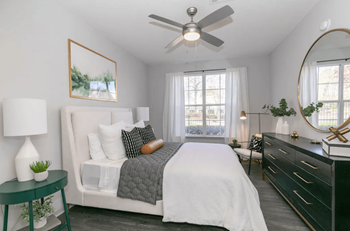 A bedroom with a white bed, a green side table, and a ceiling fan.